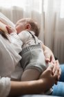 Ritagliato irriconoscibile mamma adulta in abbigliamento casual succhiare affascinante bambino mentre seduto in camera luce casa — Foto stock
