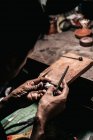 Von oben gesichtsloser Handwerker mit Metallpiercing-Säge und Silberstück bei der Arbeit am schäbigen Schreibtisch — Stockfoto