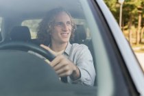 Happy young haired male looking away through open window of car while sitting at driver seat — Stock Photo