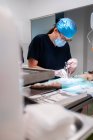 Female vet in mask and eyeglasses using medical scissors while operating feline patient on table in hospital — Stock Photo