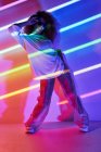 Full body stylish confident female dancer standing in neon lights and touching sunglasses in dancing studio — Stock Photo