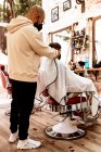 Male hairstylist in eyeglasses making haircut to adult client in hairdressing salon during COVID 19 pandemic — Stock Photo