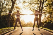 Joyeux coureuses athlétiques debout sur le chemin dans le parc et réchauffer les bras pendant l'entraînement au coucher du soleil — Photo de stock
