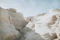 Back view anonymous female in white sundress strolling along narrow passage formed by light curvy rocks on sunny weather in Sarakiniko Greece — Stock Photo