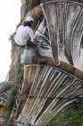 Back view full body of painter with spray paint making graffiti hanging on rope on steep rocky slope — Stock Photo