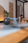 Вид сбоку подтянутой женщины в спортивном костюме, выполняющей упражнения на мяч во время тренировки в тренажерном зале пилатеса — стоковое фото