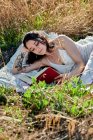 Dreamy charming brunette in white dress lying on field meadow and reading book in sunlight — Fotografia de Stock