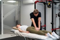 Неочікуваний чоловічий фізіотерапевт масажує ногу жінки на ліжку під час медичної процедури в лікарні — стокове фото
