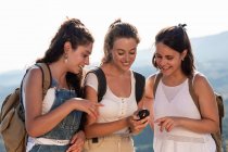 Felice giovani viaggiatori femminili in abiti estivi utilizzando bussola insieme mentre in piedi su un terreno collinare lussureggiante e soleggiato — Foto stock