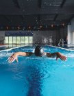 Forte nuotatore maschile in cuffia da bagno che esegue ictus di farfalla durante l'allenamento in piscina con acqua blu — Foto stock