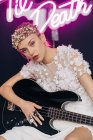 Energetische rebellische junge Frau in elegantem weißen Brautkleid und Kranz mit Gitarre in der Hand, die im Studio eine Horn-Geste mit Neonaufschrift macht — Stockfoto