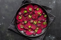 Composizione vista dall'alto di gustose fette di barbabietola preparate su teglia con peperoni verdi jalapeno e poste su asciugamano nero sul tavolo della cucina — Foto stock