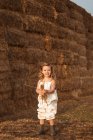 Cheerful adorable child in overalls playing with hay near straw bales in countryside — Stock Photo