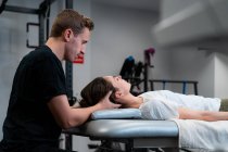 Side view of unshaven male physical therapist massaging neck of woman with closed eyes in hospital — Stock Photo
