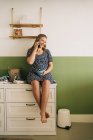 Allegra donna incinta con tazza di bevanda calda che parla sul cellulare mentre distoglie lo sguardo nella stanza della casa — Foto stock