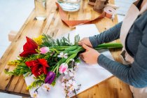 De cima cortado florista feminino irreconhecível em roupas casuais e avental arranjando buquê elegante de flores sortidas na loja — Fotografia de Stock