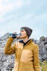Woman in warm clothes standing on high range of Peaks of Europe and drinking water — Stock Photo