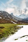 Picturesque green fields with snow in valley of Peaks of Europe under heavy cloudy sky in Spain — Stock Photo