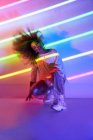 Повний стиль кузова упевнена афроамериканська танцівниця з кучерявим волоссям і сонцезахисними окулярами прикуті до камери в неонові вогні в танцювальній студії — стокове фото