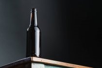 Темна скляна пляшка алкогольного напою на пофарбованому дерев'яному столі квадратної форми в домашніх умовах — стокове фото