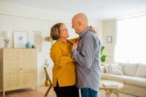 Glückliches Paar mittleren Alters, das sich zu Hause im Wohnzimmer umarmt und tanzt, während es sich zärtlich ansieht — Stockfoto