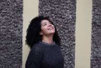 Delighted ethnic female with Afro hairstyle standing on street while look up - foto de stock