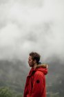 Vista laterale pensoso escursionista maschio in capispalla in piedi sulla cima della montagna in altopiani a Siviglia sul tempo nebbioso nuvoloso — Foto stock