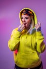 Coquettish female in street style clothes looking at camera on purple background in studio with neon illumination — Stock Photo