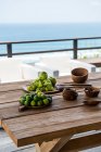 Високі кутові тарілки зі здоровими смачними зеленими лапками з яблуками та виноградом, поданими на столі з дерев'яною чашею та ложками на терасі над морем у сонячний день — стокове фото