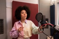 Schwarze Sängerin performt Song gegen Mikrofon mit Popfilter, während sie mit der Hand auf der Hüfte steht und sich im Tonstudio nach vorne freut — Stockfoto