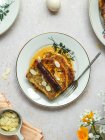 De haut de pain grillé français savoureux étant versé avec du miel et garni de flocons d'amandes servis sur l'assiette sur la table pour le petit déjeuner — Photo de stock