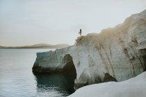 Persona irriconoscibile in piedi su una ruvida scogliera rocciosa bagnata dal tranquillo mare blu nella giornata di sole in Grecia — Foto stock