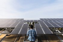 Анонимный профессиональный техник в клетчатой рубашке, проверяющий фотоэлектрические панели на солнечной электростанции в ясную солнечную погоду — стоковое фото
