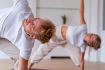 Couple in activewear standing on mats in trikonasana while doing yoga in morning and looking at each other — Photo de stock