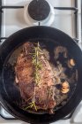 De dessus de poêle avec morceau de viande appétissante avec condiments et romarin brin de beurre fondu sur cuisinière à gaz — Photo de stock