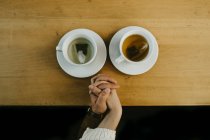 Вид зверху врожаю невпізнавана пара тримає руки, сидячи за столом з чашками гарячого чаю — стокове фото
