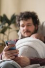 Padre adulto abrazando a un niño anónimo mientras navega por Internet en el teléfono celular en la casa durante el día - foto de stock