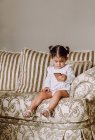 Чарівна маленька дитина сидить на дивані вдома і дивиться цікавий мультфільм на мобільний телефон — стокове фото