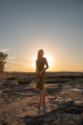 Вид збоку на молоду жінку, що стоїть на скелі під час заходу сонця і дивиться вниз — стокове фото