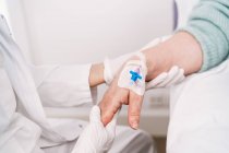 High angle of crop anonymous medic in disposable gloves putting intravenous catheter on arm of patient in hospital — Stock Photo