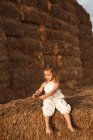 Joyeux adorable enfant en salopette jouant avec le foin assis sur des balles de paille dans la campagne — Photo de stock