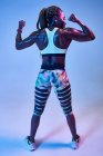 Vista posterior de atleta femenina afroamericana muscular anónima con cuerpo sudoroso mostrando bíceps sobre fondo azul - foto de stock