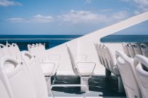 Chaises blanches vides sur le pont du bateau de croisière naviguant dans l'eau de mer bleue — Photo de stock