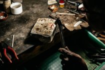 Dall'alto anonimo artigiano al banco da lavoro utilizzando torcia calda e fondendo piccoli pezzi di metallo — Foto stock
