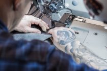 Зверху чоловічий майстер використовує швейну машину при створенні оббивки для сидіння мотоцикла в майстерні — стокове фото