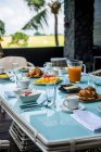 From above of comfortable wicker armchair with soft seats and cushions placed near table served with various appetizing pastries and fruits during breakfast in tropical resort — Fotografia de Stock