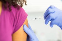 Обрезанная неузнаваемая женщина-врач в защитной форме и латексных перчатках вакцинирует анонимную афроамериканку-пациентку в клинике во время вспышки коронавируса — стоковое фото