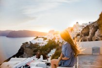 Vista trasera de una viajera irreconocible admirando Oia Village en la isla de Santorini en un día ventoso en Grecia - foto de stock