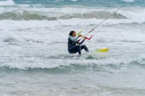 Aktive Sportlerin auf dem Kiteboard hält Kontrollstange beim Kitesurfen und schaut auf schäumenden Ozean weg — Stockfoto