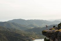 Remote view of female hiker standing with outstretched arms on edge of hill and enjoying freedom during trekking in mountains in summer — Stock Photo